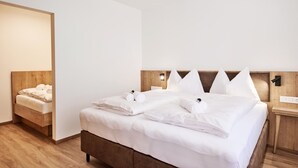 A neatly made bed with white linens and pillows, a wooden headboard, and a bedside table with a lamp. - Alpenstolz #1.08 Comfort with coolfire (Damüls)