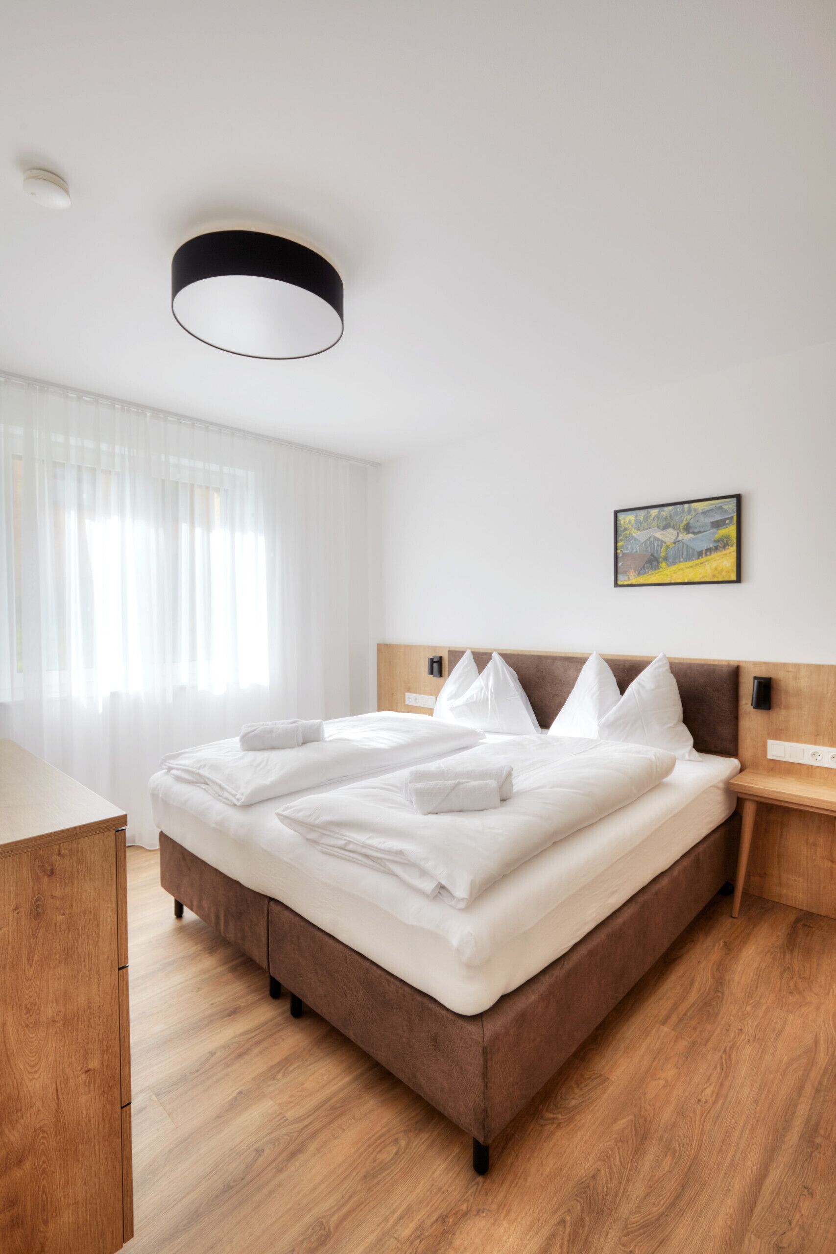 A neatly made bed with white linens, a wooden headboard, a bedside table, and a painting on the wall.