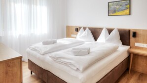 A neatly made bed with white linens, a wooden headboard, a bedside table, and a painting on the wall. - Alpenstolz #2.01 Comfort (Damüls)