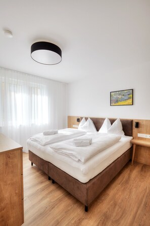 A neatly made bed with white linens, a wooden headboard, a bedside table, and a painting on the wall.