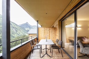 A balcony with a table and chairs, a wooden floor, and a mountain view. - Alpenstolz #2.01 Comfort (Damüls)