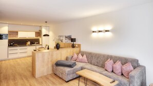 A modern living room with a sofa, a coffee table, and a kitchen area with a counter and cabinets. - Alpenstolz #2.01 Comfort (Damüls)