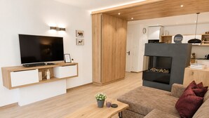 Ein modernes Wohnzimmer mit Flachbildfernseher, Holzmöbeln, einem Kamin und einem gemütlichen Sofa.