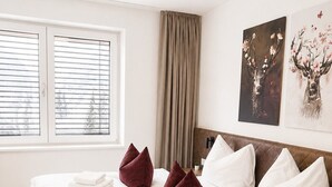Ein Hotelzimmer mit einem großen Bett, zwei Fenstern mit Jalousien, einem Vorhang und zwei an der Wand befestigten Kunstwerken.