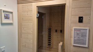 Ein Zimmer mit Holzwänden, eine Tür zu einem Badezimmer. Ein gerahmtes Bild hängt an der Wand, rechts befindet sich eine Bedienkonsole.