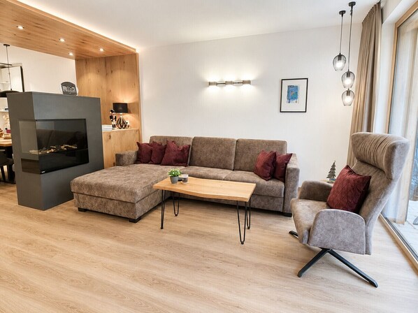 A modern living room with a sectional sofa, a wooden coffee table, a fireplace, and a dining area with a table and chairs. - Alpenstolz #2.03 Exklusive with infrared&Coolfire (Damüls)