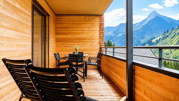 Ein Holzbalkon mit Stühlen und einem Tisch, mit Blick auf eine gebirgige Landschaft.