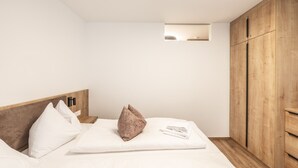 A bedroom with a bed, pillows, a wooden wardrobe, and a small window. - Alpenstolz #2.05 Comfort (Damüls)