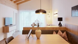 Una sala de estar moderna con techo de madera, una mesa de comedor, un jarrón con flores y un televisor sobre un mueble.