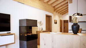 Uma sala de estar moderna com lareira, vigas de madeira no teto, uma televisão e um vaso com flores.