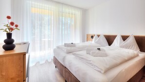 Une chambre d’hôtel avec un grand lit, du linge de lit blanc, une tête de lit en bois, une table de chevet ornée d’un vase de fleurs et des rideaux légers.