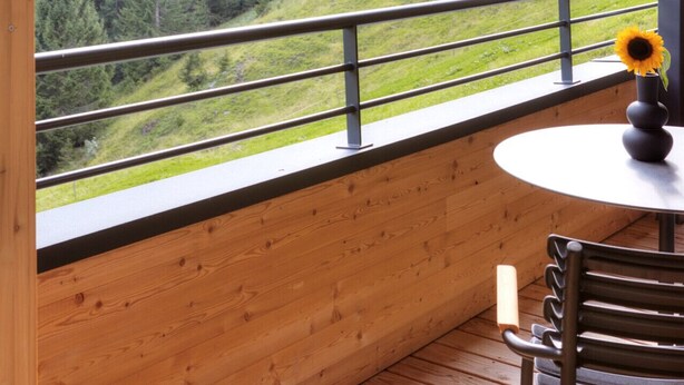 Un balcón de madera con vistas a una cadena montañosa y bosque.