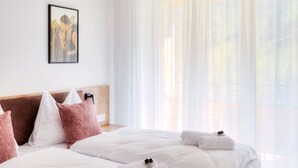 Una habitación de hotel moderna con una cama grande, ropa de cama blanca y un cabecero con almohadas rosadas.