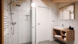 Un bagno moderno con box doccia in vetro, una porta bianca, un mobile bagno in legno con specchio e lavandino.