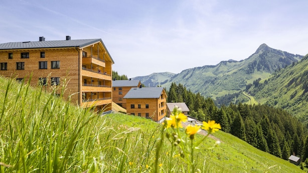 A multi-story wooden building with balconies, set against a mountainous backdrop. - Alpenstolz #3.06 Comfort with Coolfire (Damüls)