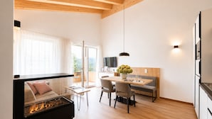 A modern living room with a fireplace, a dining area, and a kitchen with a TV. - Alpenstolz #3.06 Comfort with Coolfire (Damüls)