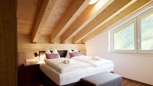 A bedroom with a wooden ceiling, a bed with white bedding, a bench, and a window with a view of trees. - Alpenstolz #3.06 Comfort with Coolfire (Damüls)