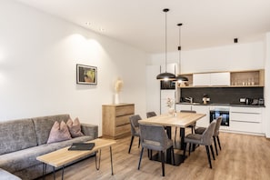 A modern living space with a sofa, dining table, chairs, and a kitchen area.