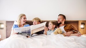 A family of four lying in bed, reading a magazine. - Alpenstolz #4.03 Comfort (Damüls)