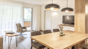 A modern dining area with a wooden table, six chairs, a vase with flowers, and a television on the wall. - Alpenstolz #4.03 Comfort (Damüls)