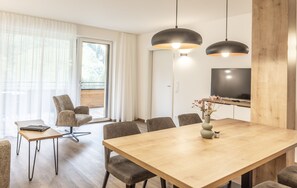A modern dining area with a wooden table, six chairs, a vase with flowers, and a television on the wall. - Alpenstolz #4.03 Comfort (Damüls)