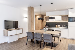 Una cocina moderna con una mesa de comedor de madera, sillas tapizadas en gris y un televisor integrado.