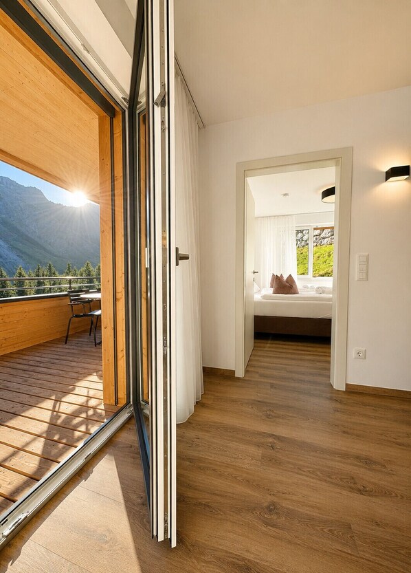 A modern interior with a wooden deck, a bedroom with a bed and curtains, and a view of mountains.
