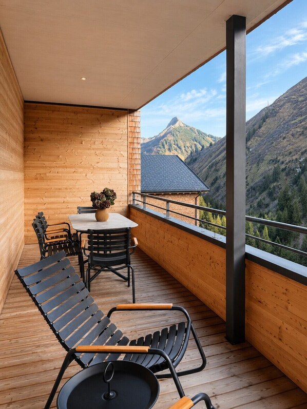 A balcony with wooden flooring, a table with chairs, and a view of mountains.