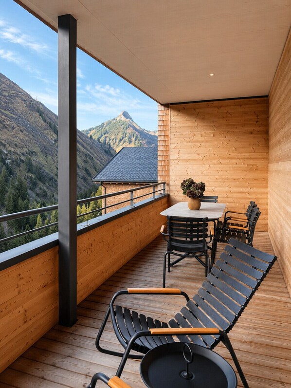 A balcony with a table and chairs, a view of mountains, and a wooden interior.
