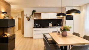 A modern kitchen with white cabinets, a black countertop, and a dining area with a wooden table and grey upholstered chairs.