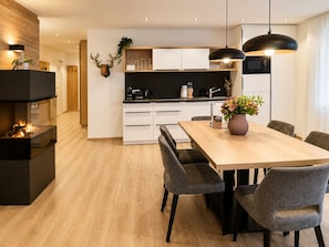 A modern kitchen with white cabinets, a black countertop, and a dining area with a wooden table and grey upholstered chairs.