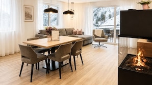 A modern living room with a dining area, a fireplace, and a balcony with a view of snow-covered trees.
