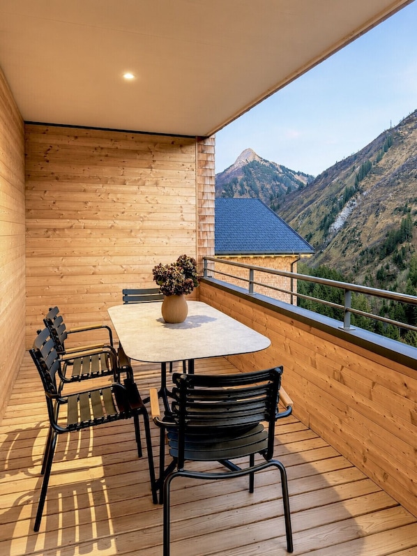 A balcony with a table and chairs, a vase with flowers, and a mountain view.