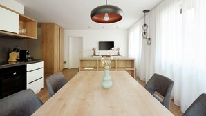 Une cuisine moderne avec des meubles en bois, un four noir et un coin repas comprenant une table en bois clair et des chaises grises.
