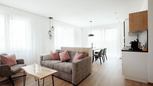 Un salon moderne avec un canapé gris, une table basse en bois et un coin repas comprenant une table et des chaises blanches.