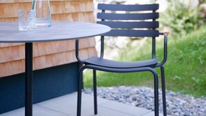 Une terrasse extérieure avec une table et une chaise, une carafe en verre et un verre.