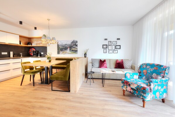 A modern kitchen with a dining area, a sofa, and a floral armchair.