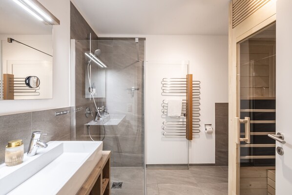 Un baño moderno con cabina de ducha de vidrio, tocador de madera y un perchero para toallas.