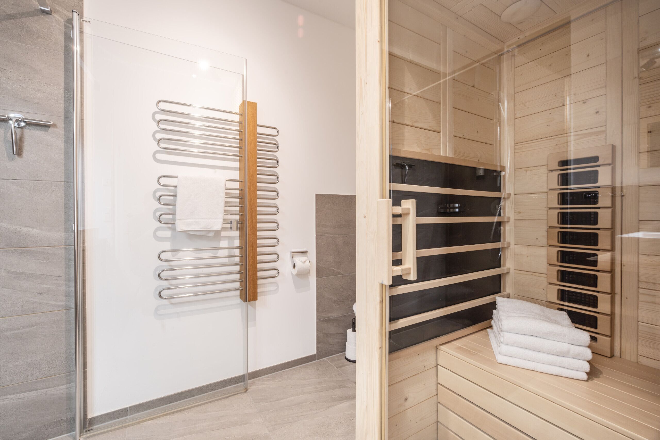 Une salle de bain moderne avec une douche à parois de verre, un porte-serviettes et un banc en bois pour sauna.