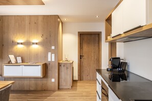 A modern kitchen with wooden cabinetry, a built-in coffee machine, and wall-mounted lighting.