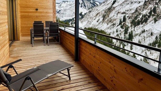 A wooden balcony with a table and chairs, overlooking a snowy mountain range. - Alpenstolz #4.09 Exklusive with coolfire (Damüls)