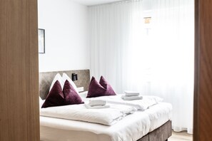 A hotel room with a bed, white linens, a headboard with a logo, and a window with sheer curtains. - Alpenstolz #4.09 Exklusive with coolfire (Damüls)