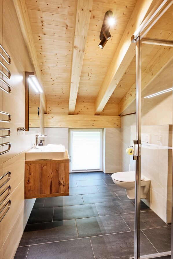 A modern bathroom with a wooden ceiling, a large window, and a glass shower enclosure.