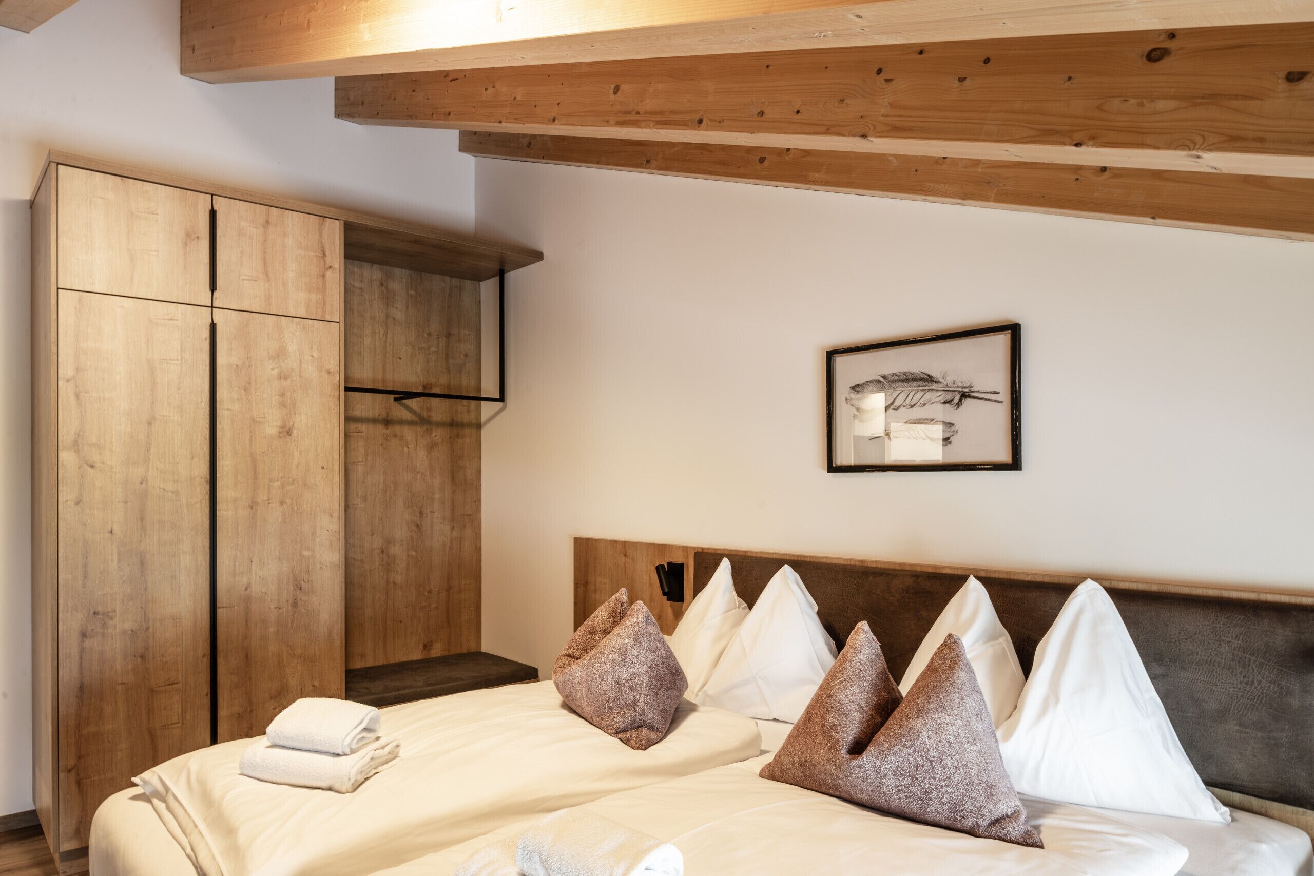 A bedroom with a wooden wardrobe, a bed with white linens, and a feather artwork on the wall.