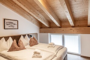 A bedroom with a wooden ceiling, a bed with pillows, a framed picture on the wall, and a window with blinds. - Alpenstolz #4.13 Comfort (Damüls)