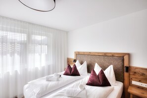 A hotel room with a bed, white linens, a wooden headboard, and a window with sheer curtains.