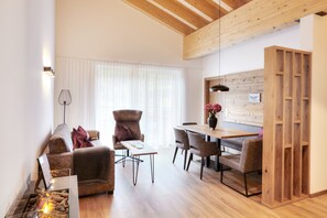 A modern living room with a sofa, armchair, dining table, and a fireplace.