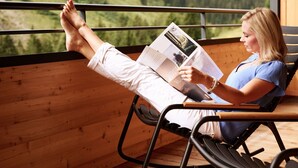 Una persona leyendo un libro en una terraza de madera con vistas a la montaña.