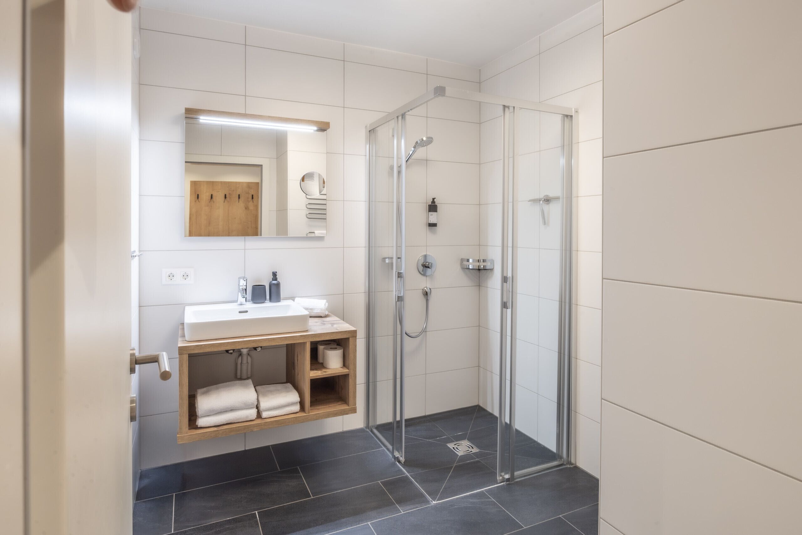 Een moderne badkamer met een douchecabine van glas, een houten wastafelmeubel met een wastafel en een spiegel erboven.