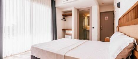 A hotel room with a bed, a wardrobe, a mirror, and a door leading to a bathroom.